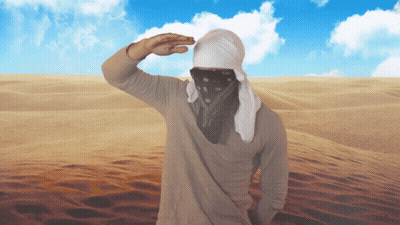 A Man Wearing A Bandana And A White Head Scarf Stands In The Desert GIF