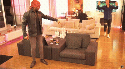 A Man Wearing A Bandana Stands In A Living Room Pointing At Something GIF