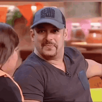 A Man Wearing A Baseball Cap And A Black Shirt Is Sitting At A Table Talking To A Woman . GIF