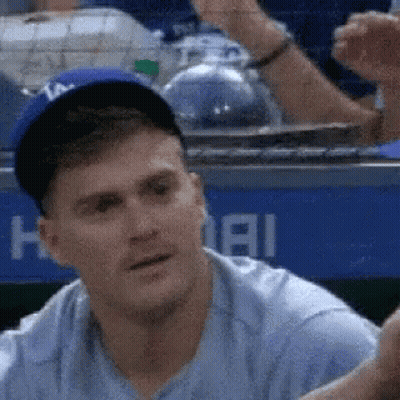 A Man Wearing A Baseball Cap And A Blue Shirt Is Sitting In The Dugout . GIF