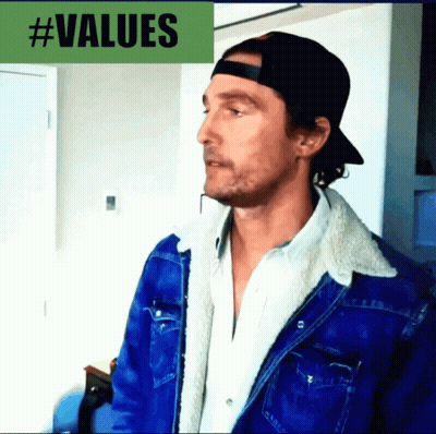 A Man Wearing A Baseball Cap And A Denim Jacket Stands In Front Of A #Values Sign GIF