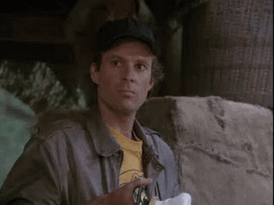 A Man Wearing A Baseball Cap And A Leather Jacket Is Standing Next To A Stone Wall . GIF