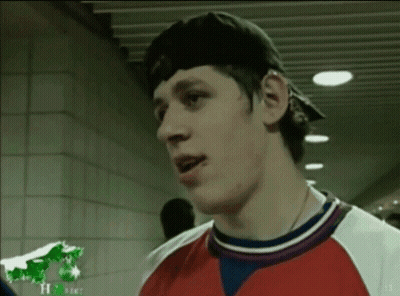 A Man Wearing A Baseball Cap And A Red White And Blue Shirt Talks To Another Man GIF