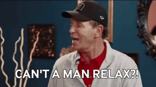 A Man Wearing A Baseball Cap And A Sweater Is Saying " Can 'T A Man Relax ? " GIF