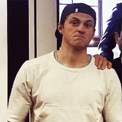 A Man Wearing A Baseball Cap And A White Shirt Is Making A Face GIF