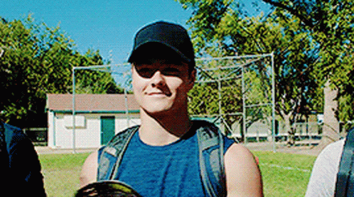A Man Wearing A Baseball Cap And Sunglasses Is Standing In A Field . GIF