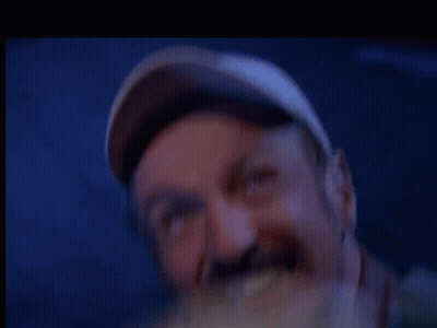 A Man Wearing A Baseball Cap Is Eating A Sandwich In A Blurry Photo . GIF
