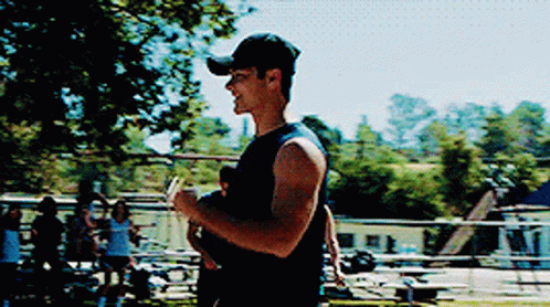 A Man Wearing A Baseball Cap Is Holding A Baby In His Arms . GIF