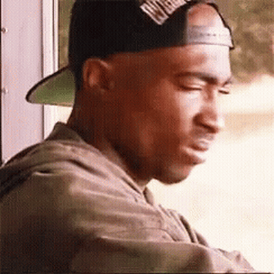 A Man Wearing A Baseball Cap Is Looking Out A Window . GIF
