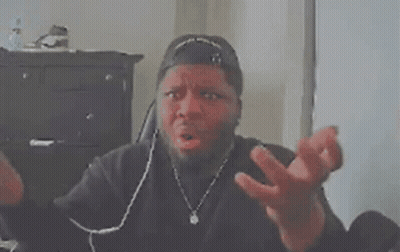 A Man Wearing A Baseball Cap Is Sitting At A Desk With His Hands Folded In Front Of His Face . GIF