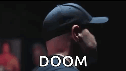 A Man Wearing A Baseball Cap Is Standing In A Dark Room With The Word Doom Behind Him . GIF