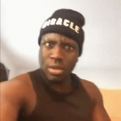 A Man Wearing A Beanie And A Black Tank Top Is Making A Funny Face . GIF