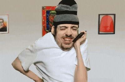 A Man Wearing A Beanie And A White Shirt Is Blowing Into A Straw GIF