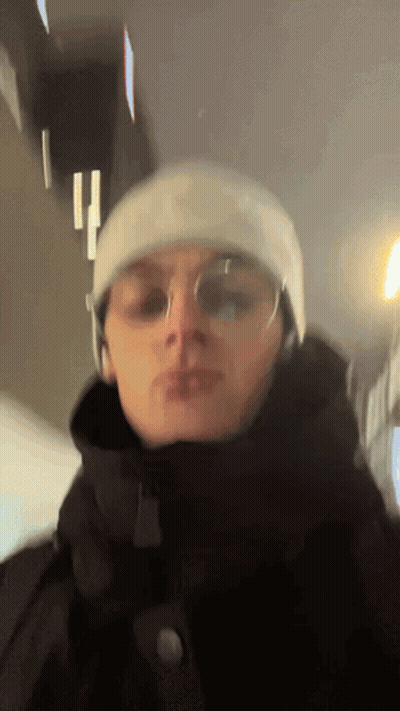 A Man Wearing A Beanie And Glasses Is Standing In A Dark Room GIF