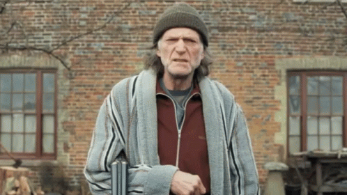 A Man Wearing A Beanie And Striped Robe Is Standing In Front Of A Brick Wall GIF