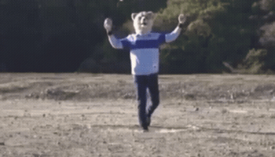 A Man Wearing A Bear Mask Is Running In A Field . GIF