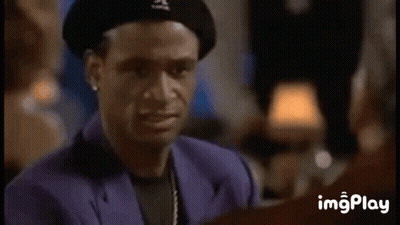 A Man Wearing A Beret And A Purple Suit Is Smiling While Talking To Another Man . GIF