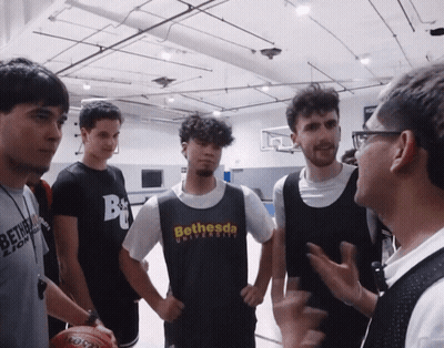 A Man Wearing A Bethesda University T-Shirt Talks To A Group Of Young Men GIF