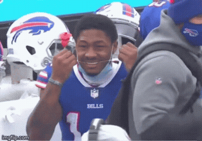 A Man Wearing A Bills Jersey Is Smiling And Putting On A Mask GIF