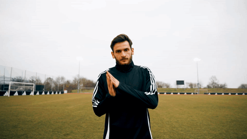 A Man Wearing A Black Adidas Jacket Is Standing On A Soccer Field GIF