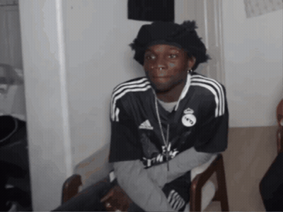 A Man Wearing A Black Adidas Shirt Is Sitting In A Chair GIF
