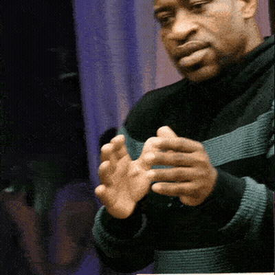 A Man Wearing A Black And Green Striped Sweater Holds His Hands Together GIF