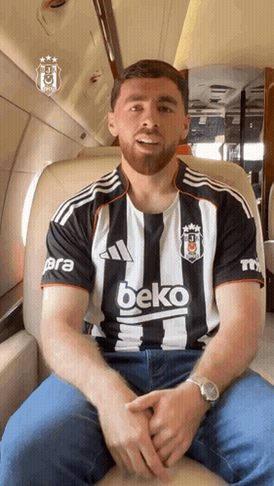 A Man Wearing A Black And White Beko Shirt Sits On A Plane GIF