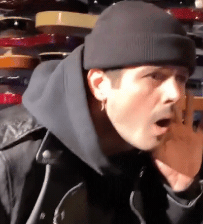 A Man Wearing A Black Beanie And A Black Jacket Is Standing In Front Of A Shelf . GIF