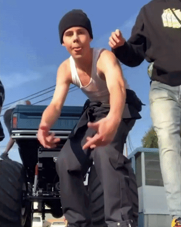 A Man Wearing A Black Beanie And A White Tank Top Stands Next To A Truck GIF