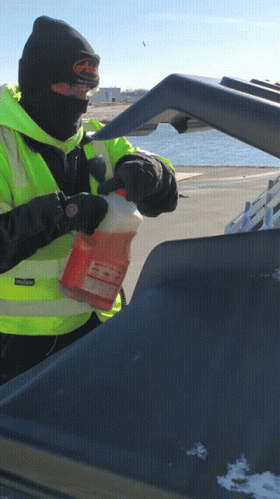 A Man Wearing A Black Beanie And A Yellow Vest Holds A Gallon Of Orange Liquid In His Hand GIF