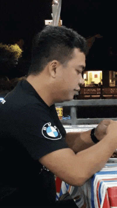 A Man Wearing A Black Bmw Shirt Sits At A Table At Night GIF