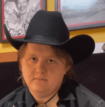 A Man Wearing A Black Cowboy Hat And A Star On His Shirt GIF