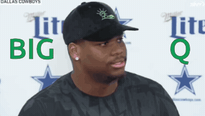 A Man Wearing A Black Hat And A Black Shirt Is Standing In Front Of A Sign That Says Dallas Cowboys GIF