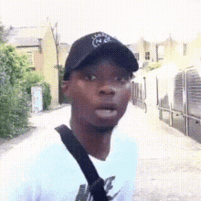 A Man Wearing A Black Hat And A White Shirt Is Standing On A Sidewalk . GIF