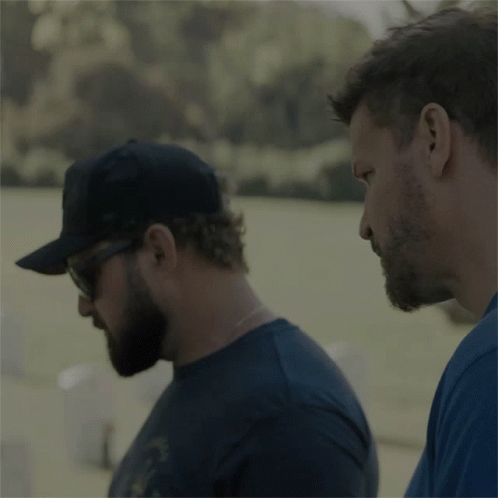 A Man Wearing A Black Hat And Sunglasses Holds Another Man 'S Shoulder GIF