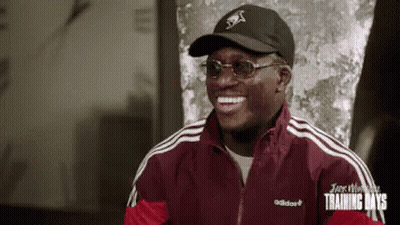 A Man Wearing A Black Hat And Sunglasses Is Smiling . GIF