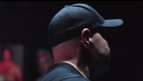 A Man Wearing A Black Hat And Sunglasses Looks To His Left GIF