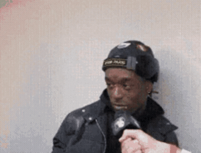 A Man Wearing A Black Hat Is Being Interviewed By A Reporter GIF