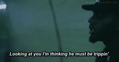 A Man Wearing A Black Hat Is Looking At Another Man While Talking . GIF