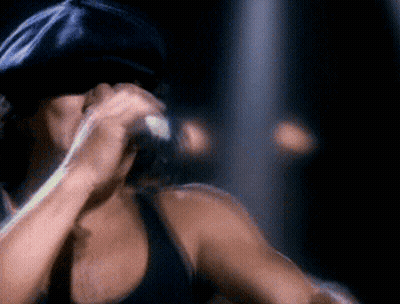 A Man Wearing A Black Hat Is Singing Into A Microphone GIF