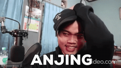 A Man Wearing A Black Hat Is Standing In Front Of A Microphone And The Word Anjing Is On The Screen Behind Him GIF