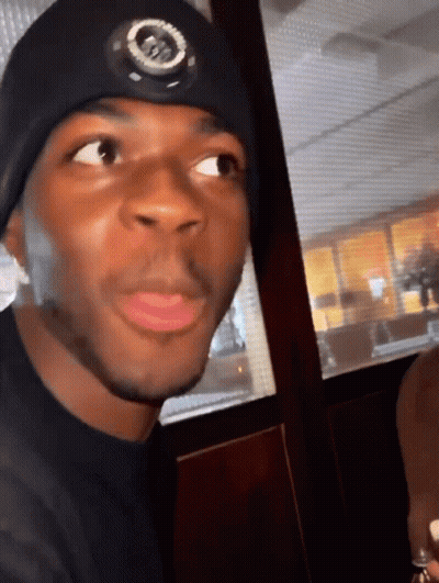A Man Wearing A Black Hat With A Circle On It Looks At The Camera GIF