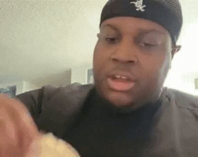 a man wearing a black hat with the letter x on it is eating a sandwich .