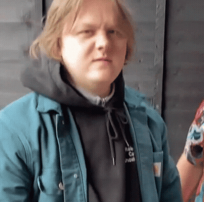 A Man Wearing A Black Hoodie And A Blue Jacket Looks At The Camera . GIF