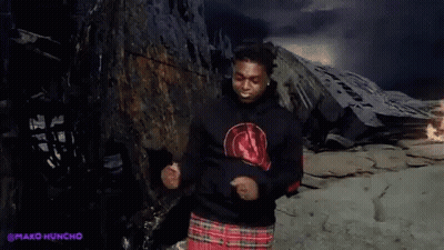 A Man Wearing A Black Hoodie And A Plaid Skirt Is Dancing In Front Of A Mountain . GIF