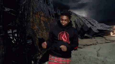 A Man Wearing A Black Hoodie And A Plaid Skirt Is Dancing In Front Of A Mountain . GIF