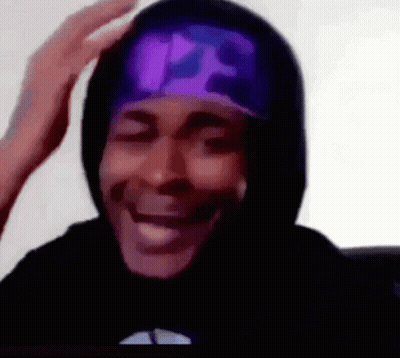 A Man Wearing A Black Hoodie And A Purple Hat Is Smiling And Touching His Head . GIF
