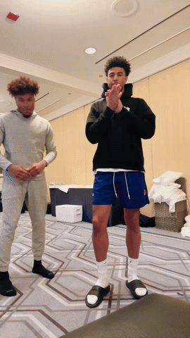 A Man Wearing A Black Hoodie And Blue Shorts Is Standing Next To Another Man GIF