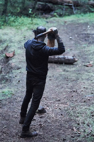 A Man Wearing A Black Hoodie Is Holding An Axe Over His Head GIF