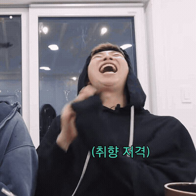 A Man Wearing A Black Hoodie Is Laughing In Front Of A Window With Korean Writing On The Bottom Right GIF